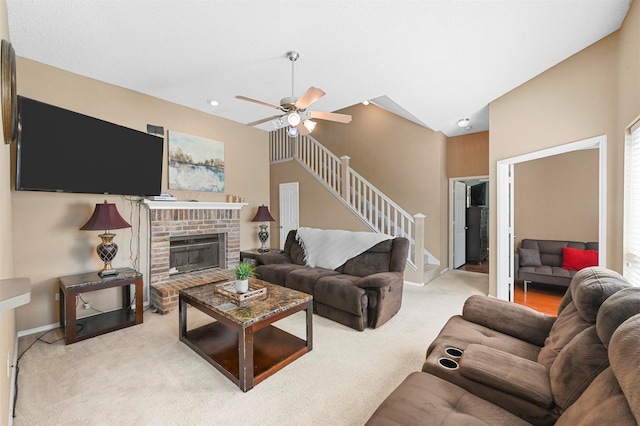 living room with ceiling fan, vaulted ceiling, a brick fireplace, and light carpet