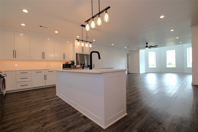 kitchen with ceiling fan, white cabinets, hanging light fixtures, a center island with sink, and dark wood-type flooring