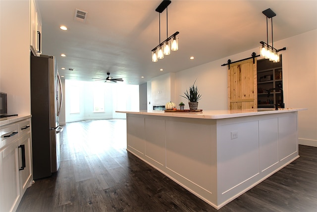 kitchen featuring a large island with sink, stainless steel fridge, a barn door, and white cabinetry