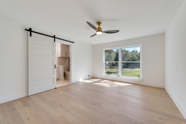 unfurnished bedroom featuring ceiling fan, light hardwood / wood-style flooring, ensuite bath, and a barn door