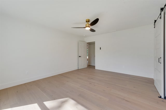 empty room with a barn door, light hardwood / wood-style floors, and ceiling fan