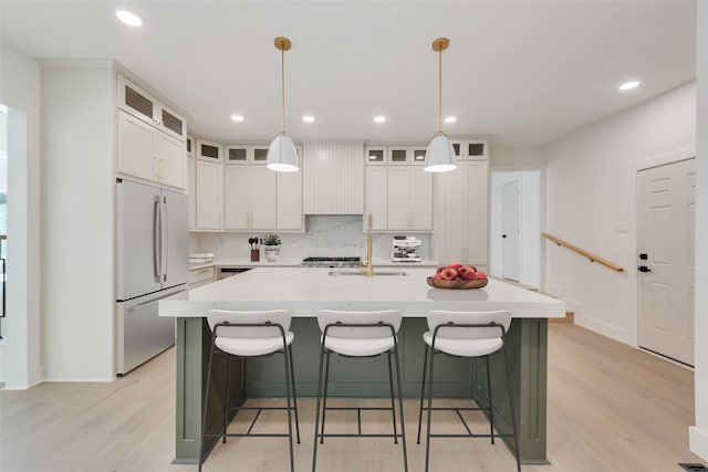 kitchen featuring pendant lighting, stainless steel refrigerator, light hardwood / wood-style flooring, and an island with sink