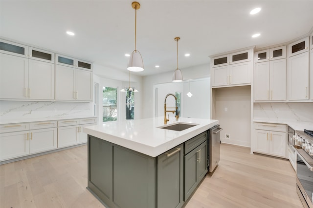 kitchen featuring light hardwood / wood-style floors, sink, an island with sink, white cabinetry, and decorative light fixtures