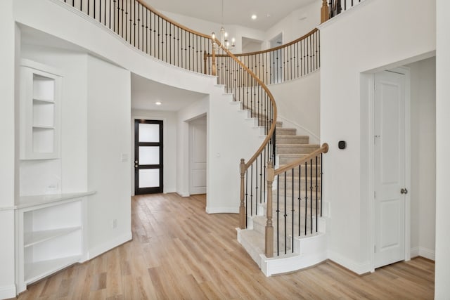foyer entrance with a towering ceiling, stairway, wood finished floors, and baseboards