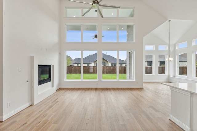 unfurnished living room with ceiling fan with notable chandelier, a high ceiling, and light wood-type flooring