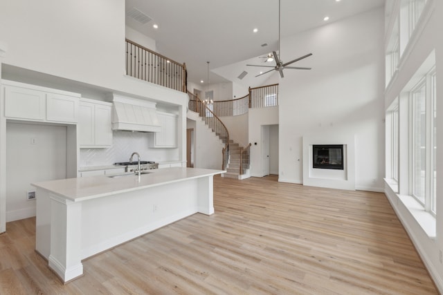 kitchen featuring custom exhaust hood, a kitchen island with sink, ceiling fan, high vaulted ceiling, and white cabinets