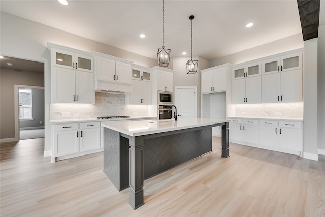 kitchen featuring pendant lighting, light hardwood / wood-style floors, white cabinetry, stainless steel appliances, and a center island with sink