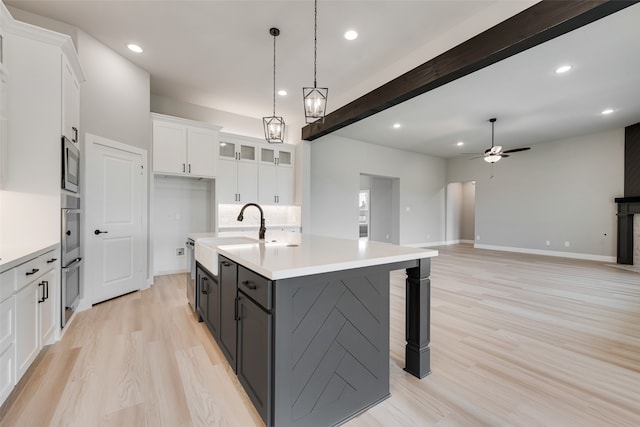 kitchen featuring hanging light fixtures, white cabinetry, beam ceiling, ceiling fan, and a kitchen island with sink