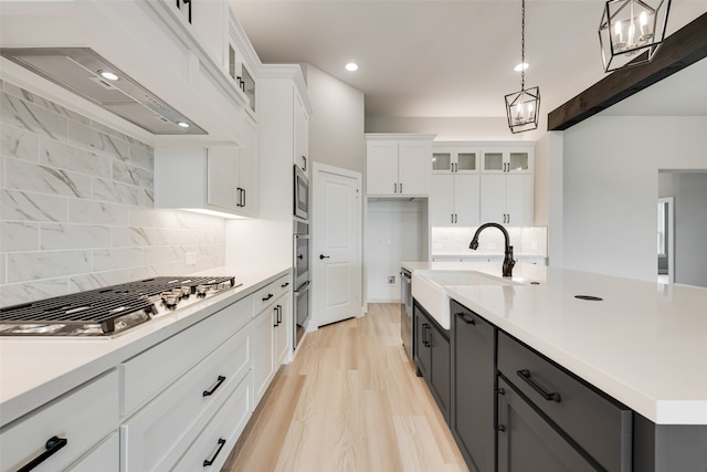 kitchen with white cabinets, decorative light fixtures, stainless steel appliances, range hood, and decorative backsplash