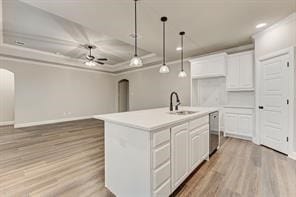 kitchen with ceiling fan, white cabinets, an island with sink, and hanging light fixtures