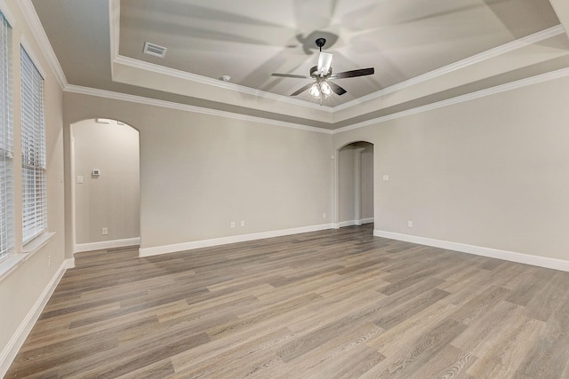 empty room with wood-type flooring, ceiling fan, a raised ceiling, and crown molding