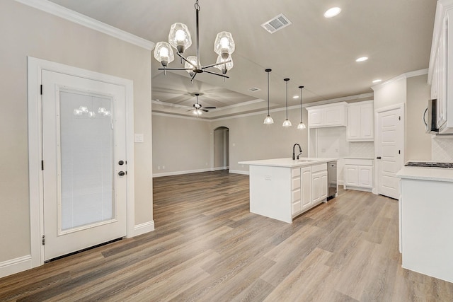 kitchen with decorative backsplash, white cabinetry, ceiling fan with notable chandelier, a center island with sink, and sink