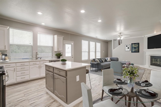 kitchen featuring sink, white cabinetry, a kitchen island, ornamental molding, and ceiling fan