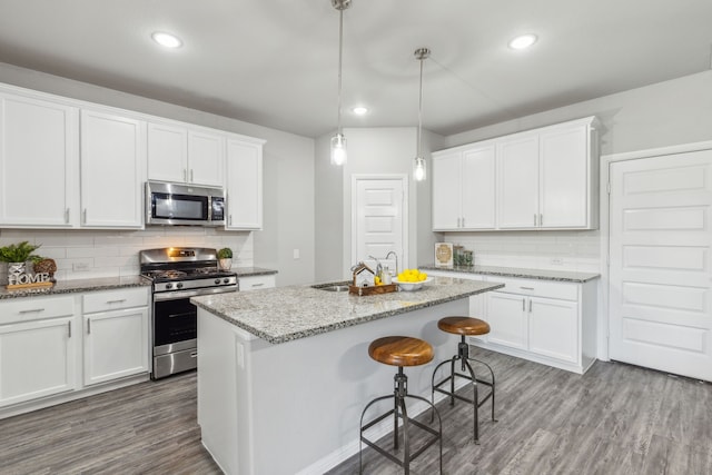 kitchen with appliances with stainless steel finishes, hanging light fixtures, white cabinetry, tasteful backsplash, and wood-type flooring