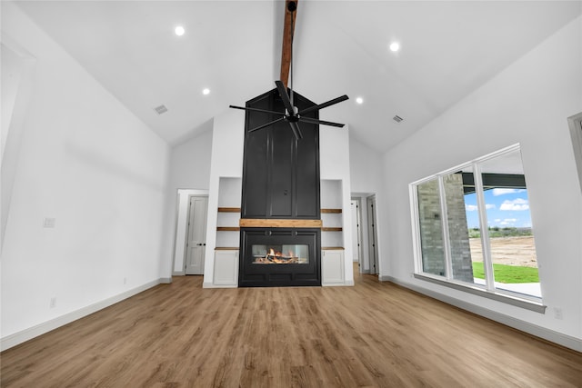 unfurnished living room with ceiling fan, beamed ceiling, a multi sided fireplace, light hardwood / wood-style flooring, and high vaulted ceiling