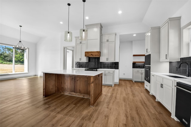 kitchen featuring a kitchen island, decorative light fixtures, vaulted ceiling, sink, and black appliances