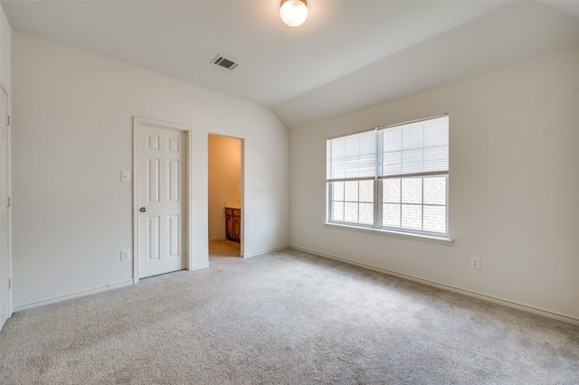 unfurnished bedroom featuring light carpet, vaulted ceiling, a closet, and ensuite bath