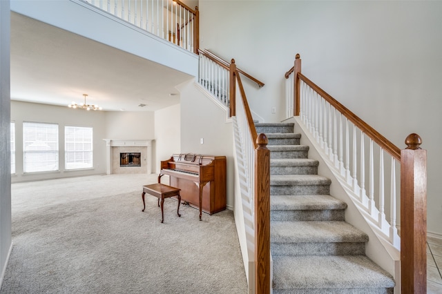 stairs featuring a notable chandelier, a high ceiling, carpet floors, and a fireplace