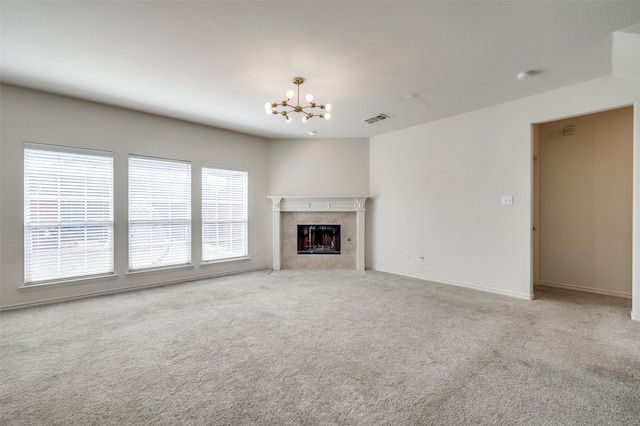 unfurnished living room with a tiled fireplace, a chandelier, and light colored carpet