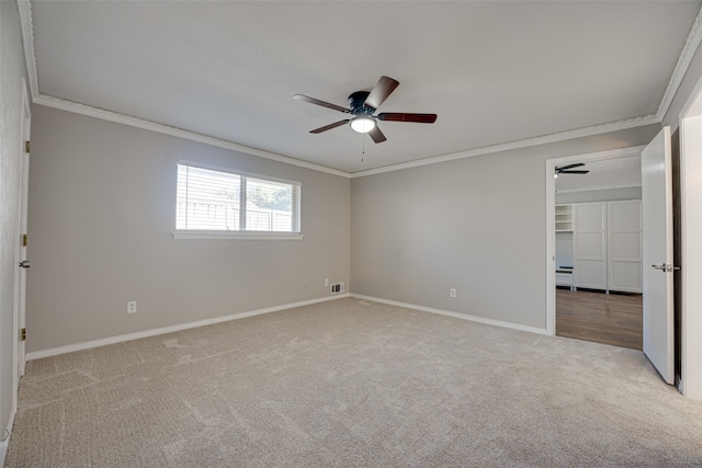 unfurnished bedroom with a closet, light colored carpet, a walk in closet, ornamental molding, and ceiling fan