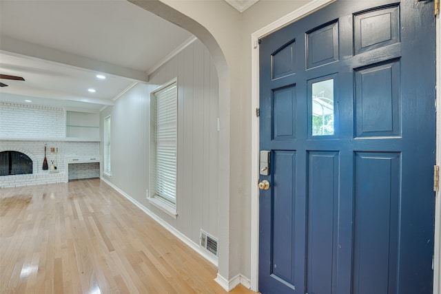 entrance foyer with light wood-type flooring, ornamental molding, ceiling fan, and a brick fireplace