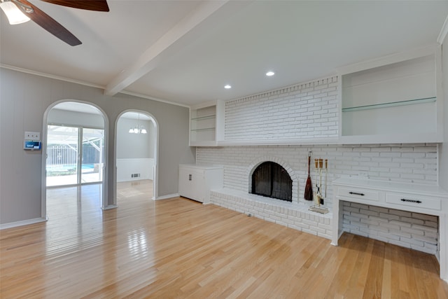 unfurnished living room featuring light hardwood / wood-style floors, beamed ceiling, a brick fireplace, crown molding, and ceiling fan