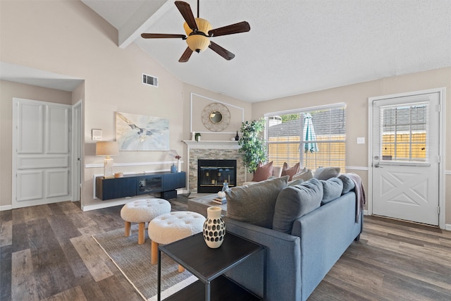 living room with ceiling fan, beamed ceiling, a stone fireplace, a textured ceiling, and dark hardwood / wood-style floors