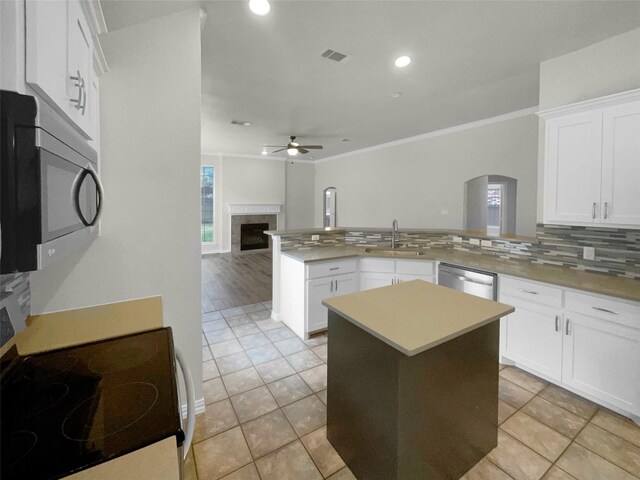 kitchen with ceiling fan, white cabinets, stainless steel appliances, and a tiled fireplace