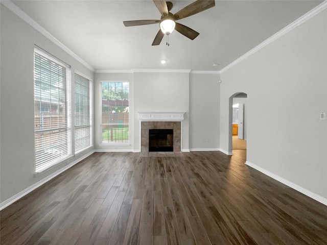 unfurnished living room with ornamental molding, a tiled fireplace, dark hardwood / wood-style flooring, and ceiling fan