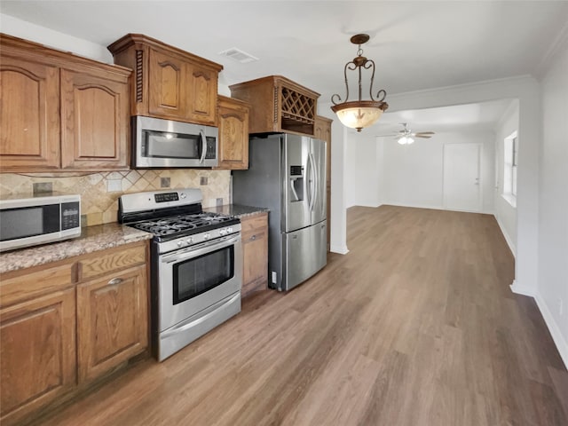 kitchen with pendant lighting, light hardwood / wood-style floors, appliances with stainless steel finishes, ornamental molding, and ceiling fan