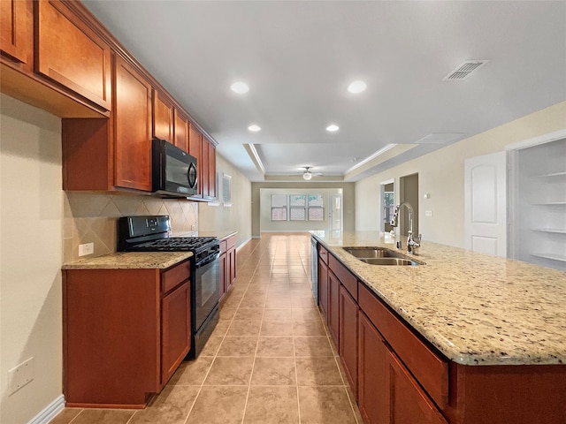 kitchen featuring light stone counters, a kitchen island with sink, sink, backsplash, and black appliances