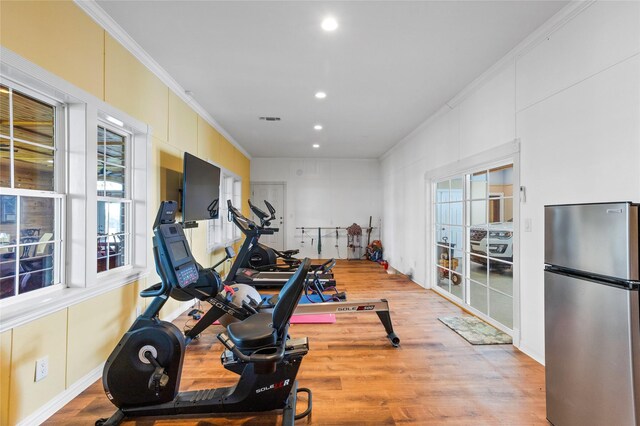 workout area with a healthy amount of sunlight, light wood-type flooring, and ornamental molding