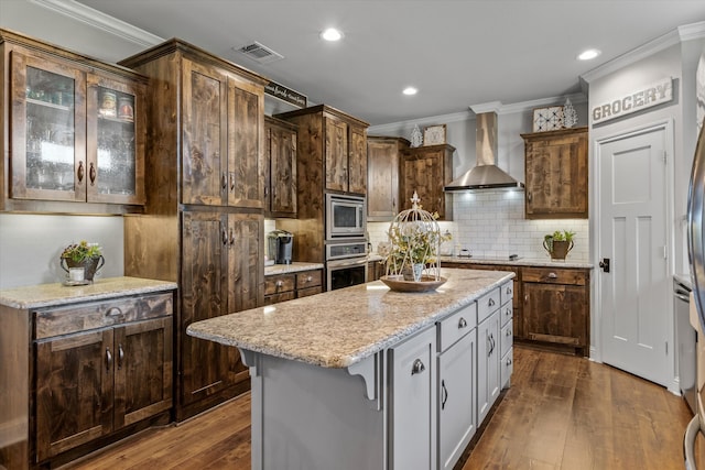 kitchen featuring light stone counters, dark wood-type flooring, a kitchen island, wall chimney exhaust hood, and stainless steel appliances