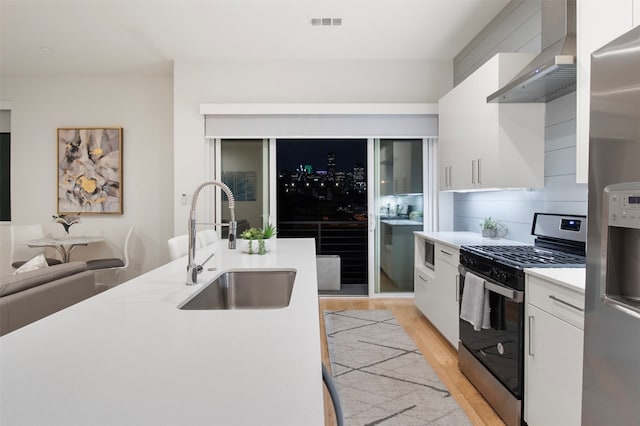 kitchen featuring wall chimney exhaust hood, stainless steel appliances, white cabinets, and light wood-type flooring