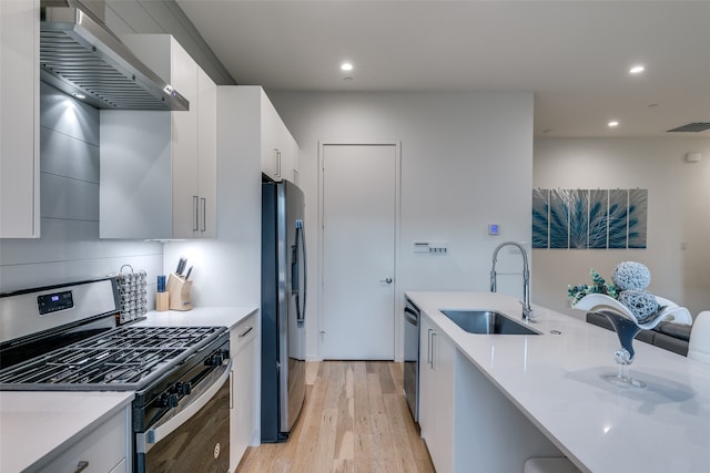 kitchen featuring sink, wall chimney range hood, white cabinetry, stainless steel appliances, and light wood-type flooring