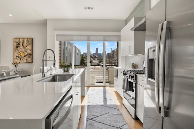 kitchen with light hardwood / wood-style floors, white cabinetry, stainless steel appliances, a kitchen island with sink, and sink