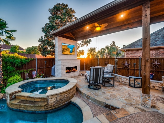 pool at dusk featuring an outdoor fireplace, an in ground hot tub, and a patio area