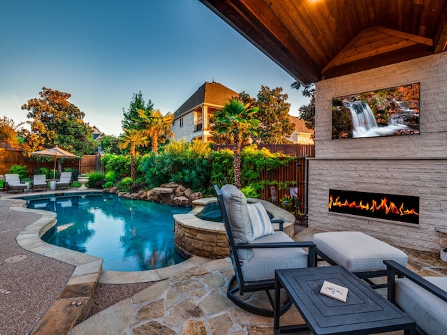 pool at dusk with a patio, an outdoor stone fireplace, and an in ground hot tub