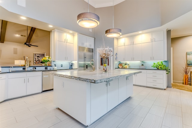 kitchen featuring appliances with stainless steel finishes, tasteful backsplash, beam ceiling, a kitchen island with sink, and sink