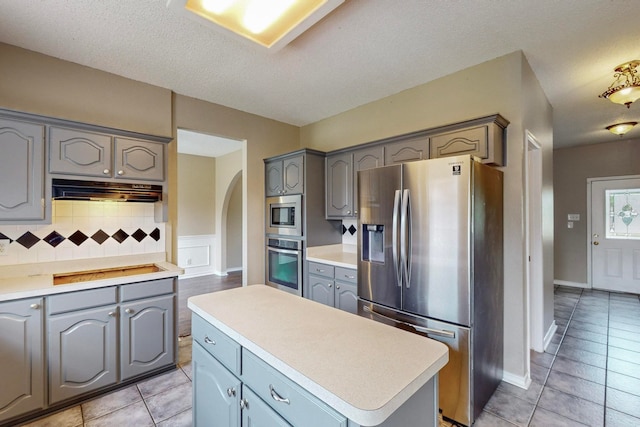 kitchen featuring tasteful backsplash, a textured ceiling, gray cabinets, stainless steel appliances, and a center island