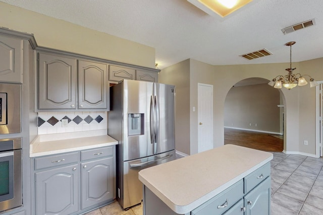 kitchen featuring gray cabinets, a kitchen island, an inviting chandelier, stainless steel appliances, and decorative backsplash