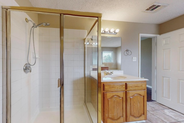 bathroom featuring tile patterned flooring, a textured ceiling, walk in shower, and vanity