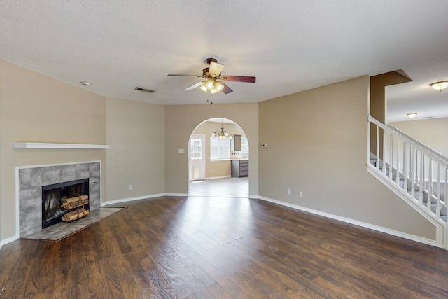 unfurnished living room with ceiling fan, a textured ceiling, a fireplace, and dark hardwood / wood-style flooring