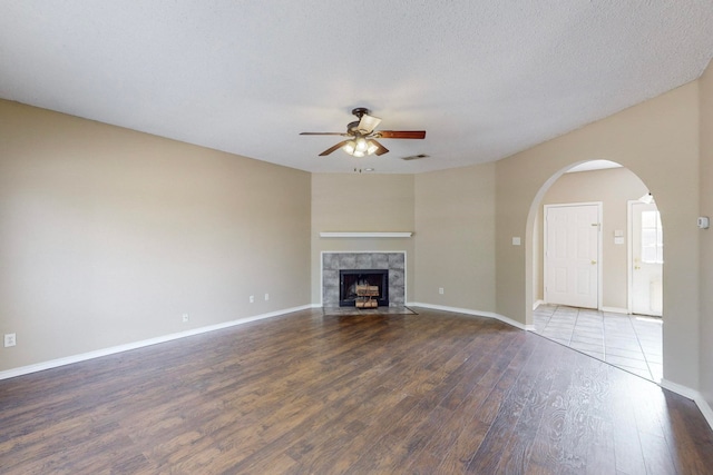 unfurnished living room featuring ceiling fan, a textured ceiling, wood-type flooring, and a tile fireplace