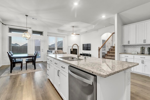 kitchen with pendant lighting, dishwasher, a kitchen island with sink, white cabinets, and light hardwood / wood-style flooring