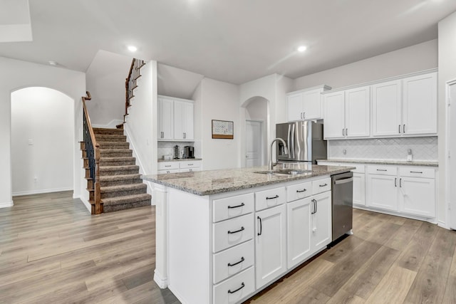 kitchen featuring a kitchen island with sink, light stone countertops, light wood-type flooring, white cabinetry, and stainless steel appliances