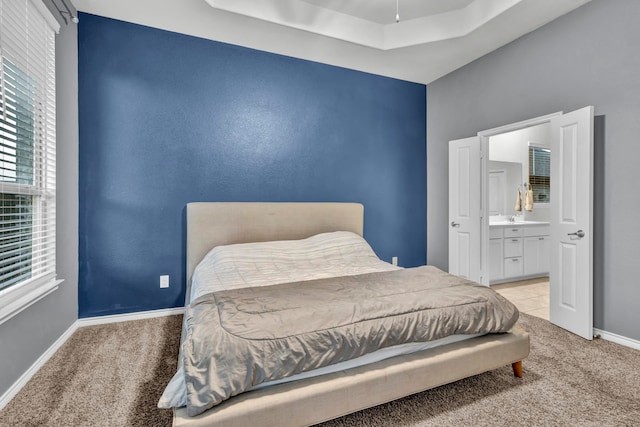 bedroom with connected bathroom, light colored carpet, and a raised ceiling