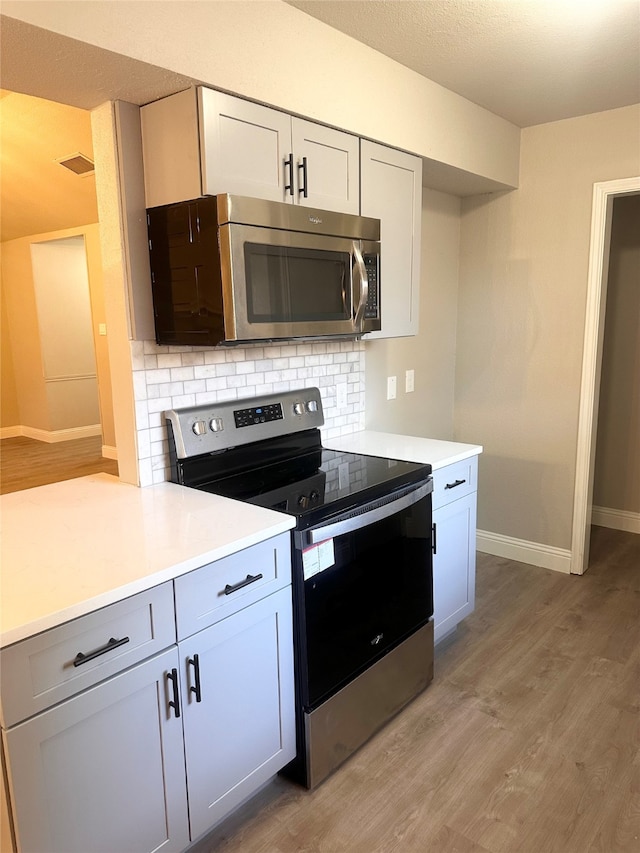 kitchen with white cabinets, stainless steel appliances, light hardwood / wood-style floors, and decorative backsplash