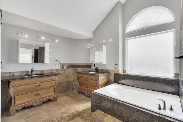 bathroom with vanity, tiled bath, vaulted ceiling, and a textured ceiling