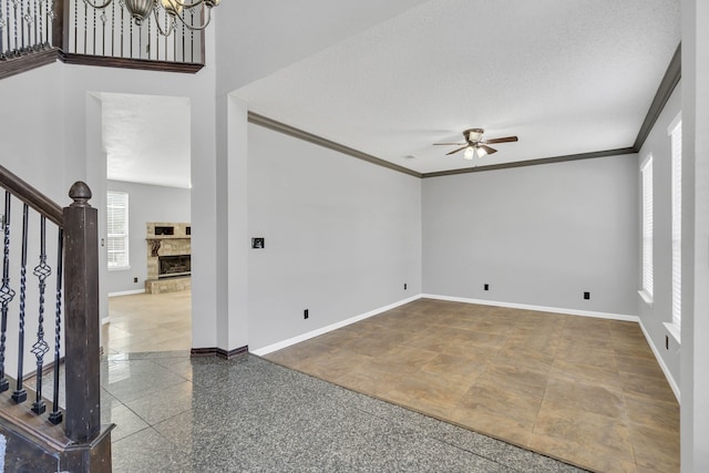 spare room featuring ornamental molding, a textured ceiling, ceiling fan with notable chandelier, and a fireplace